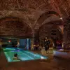 Mulher a relaxar numa piscina iluminada dentro de um spa histórico com arquitetura em tijolo e iluminação acolhedora.