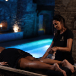 Una terapeuta aplica crema exfoliante a las piernas de una clienta en el spa In Acqua Veritas, promoviendo la renovación y el bienestar en un entorno de lujo.